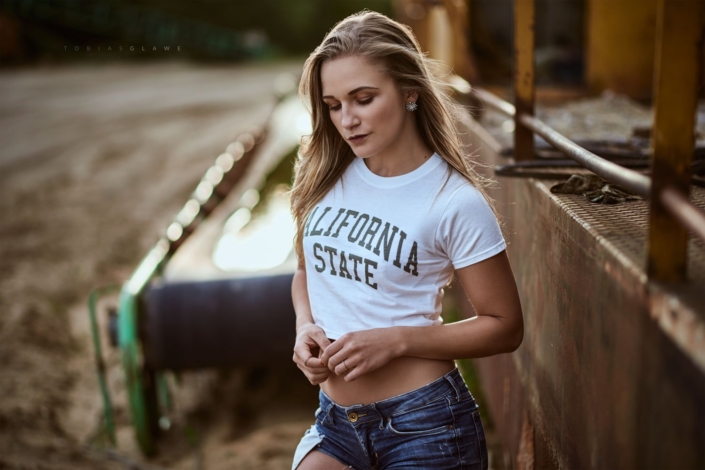 Eine junge Frau steht vor einer Holzverschalung und trägt ein T-Shirt mit der Aufschrift California State.