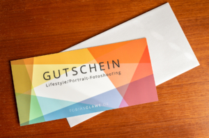 Gutschein für ein Lifestyle/Portrait-Fotoshooting auf einer weißen Hülle vor einem Holzhintergrund.